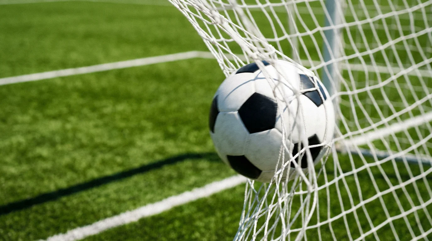 Rete di una porta da calcio vista da dietro con un pallone che entra in rete su un campo in erba verde
